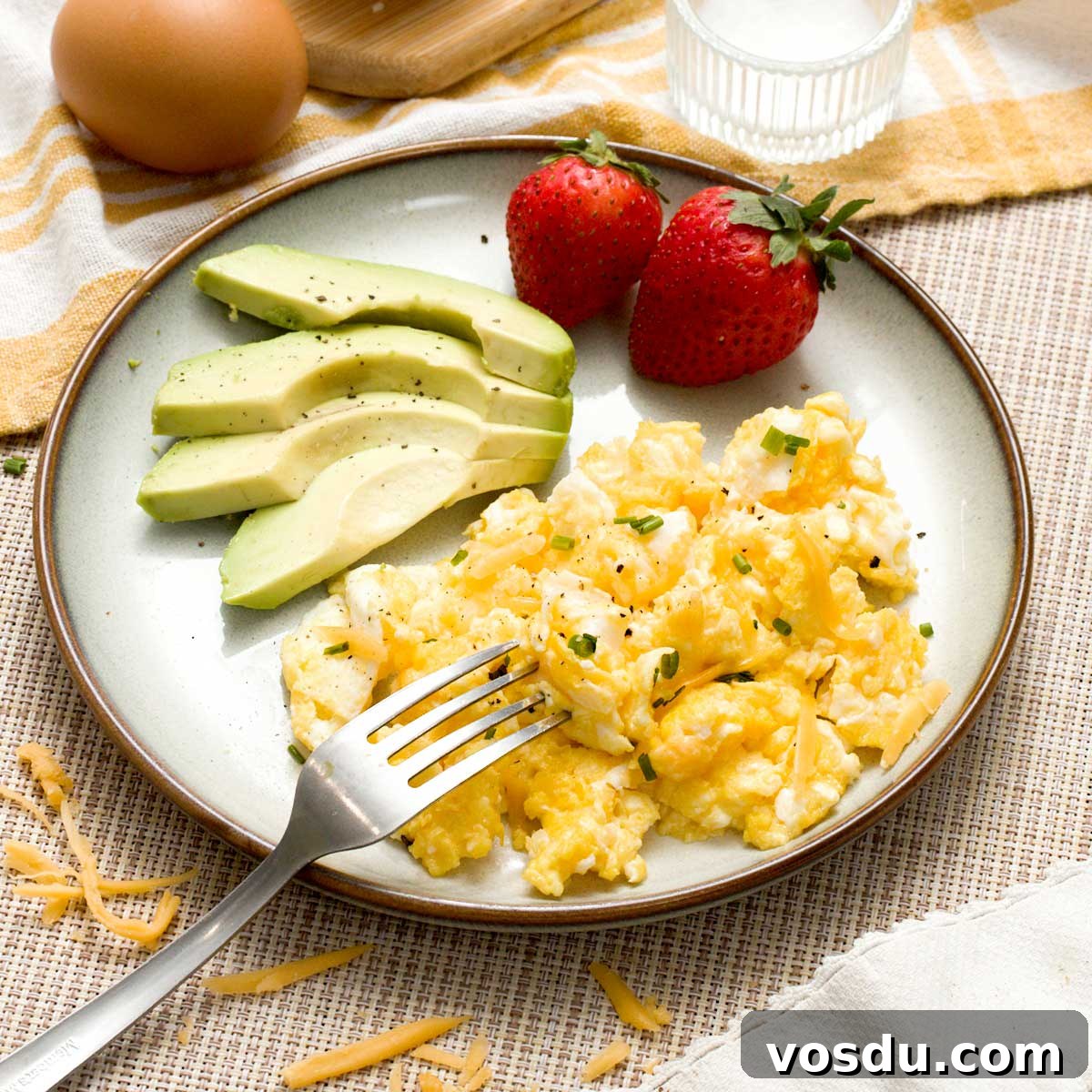 A plate of fluffy scrambled eggs with strawberries and avocado.