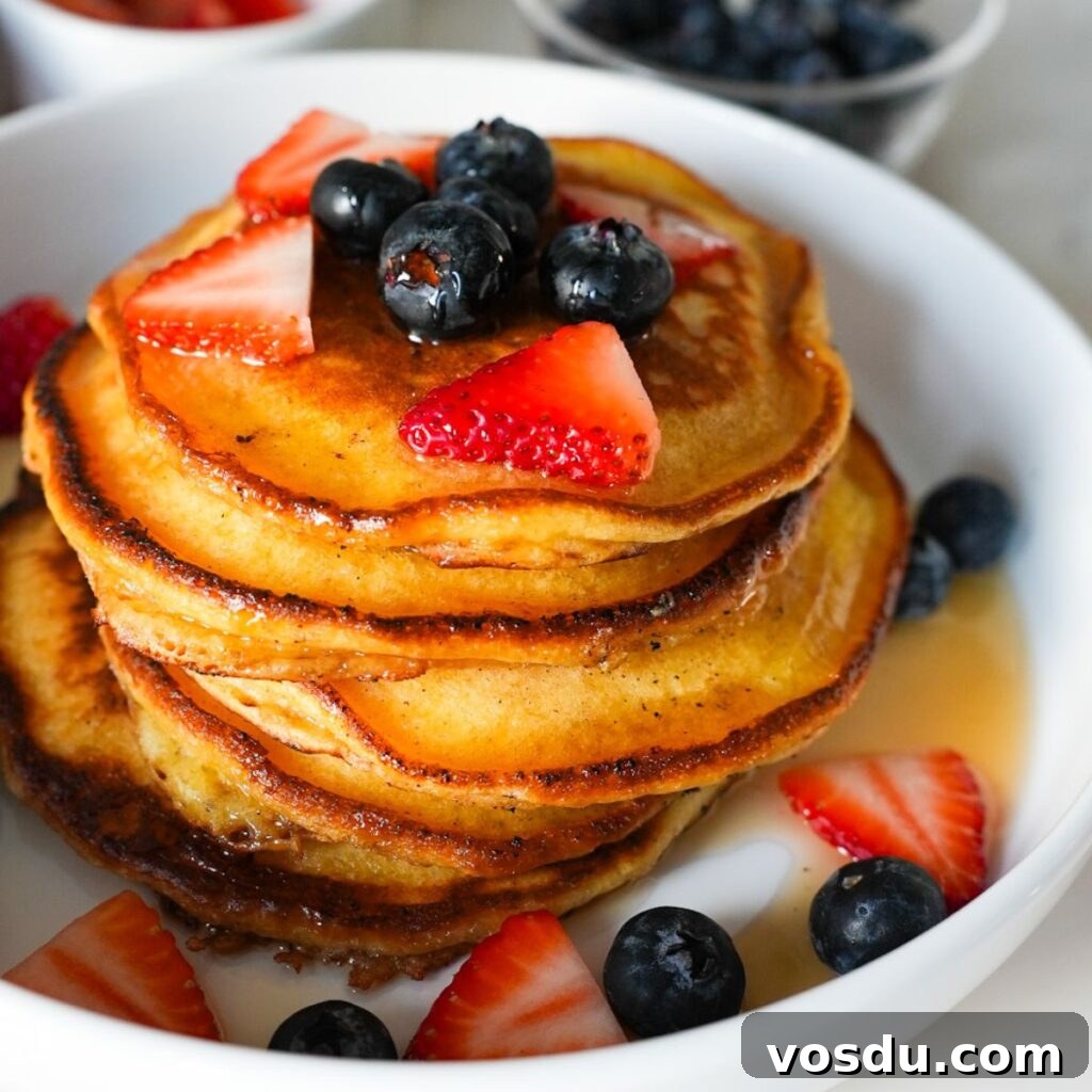 A stack of fluffy lemon ricotta pancakes topped with blueberries, strawberries and drizzled with maple syrup.