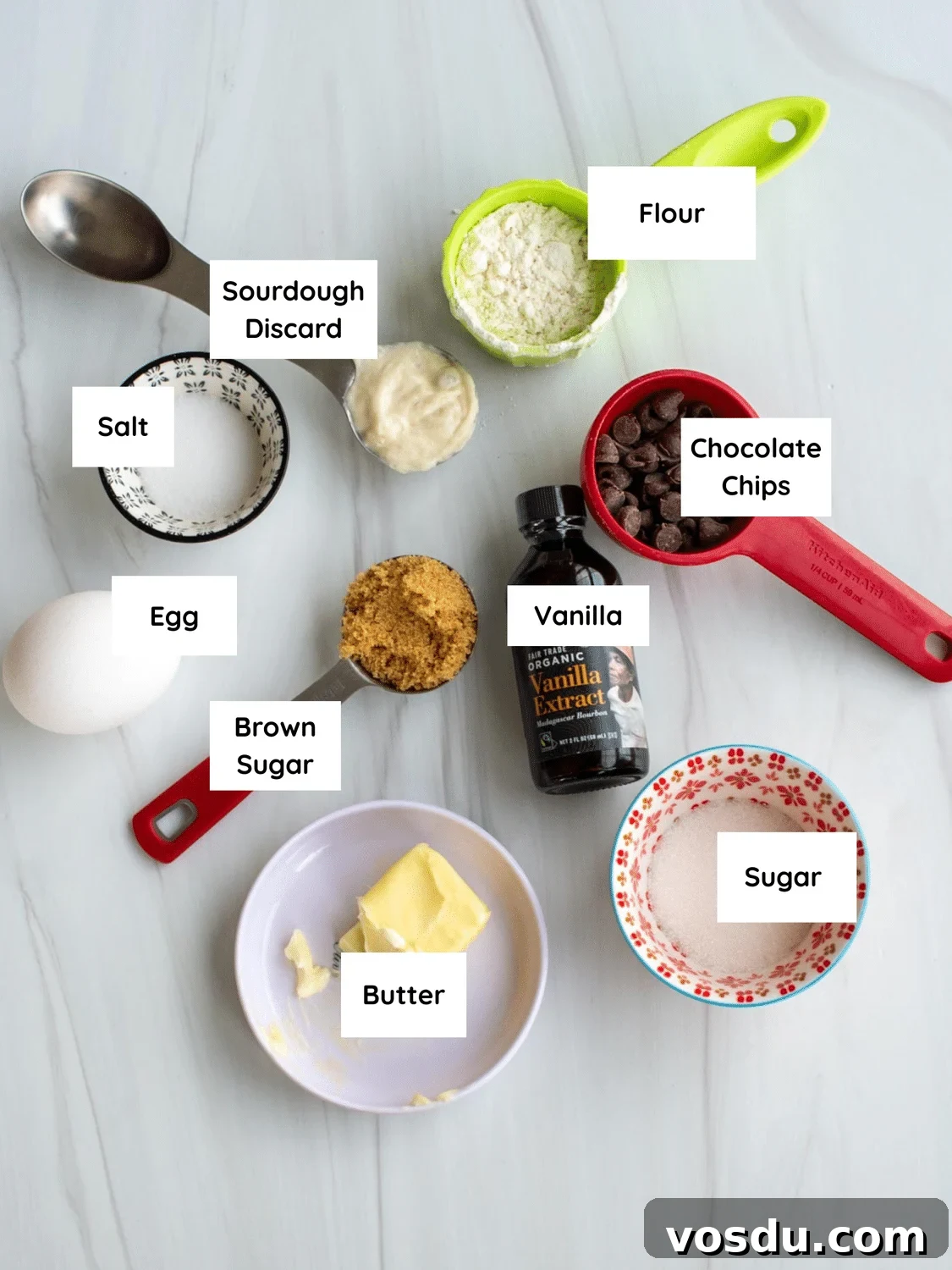 Sourdough Mug Cookie Recipe: Quick Single-Serve Treat 3 Flat lay of ingredients for a sourdough cookie in a mug, including sourdough discard, flour, chocolate chips, butter, egg, brown sugar, granulated sugar, vanilla, and salt, each labeled.