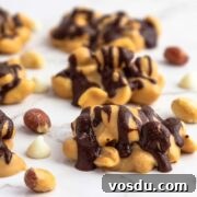 Snickers keto fat bombs are low-carb candy clusters on white marble background with scattered peanuts.