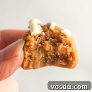 A hand holding a peanut butter cookie fat bomb with a bite out of it.