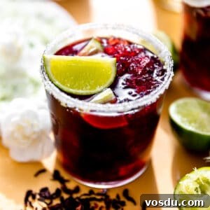 Hibiscus margarita in a glass rimmed with sugar and garnished with a lime wedge.