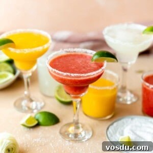 Frozen fruit margaritas lined up with mango, strawberry, and lime, with wedges of limes surrounding.