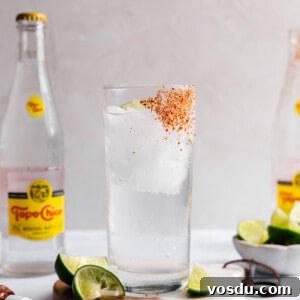A glass cup with tajin on the side and ice with clear liquid and a lime wedge inside.