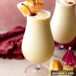 Glasses filled with smooth and creamy frozen pina colada topped with dark red cherries and wedges of pineapple.