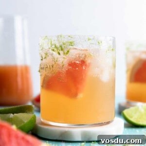 Glass on a coaster filled with grapefruit paloma on ice and a wedge of fresh grapefruit.