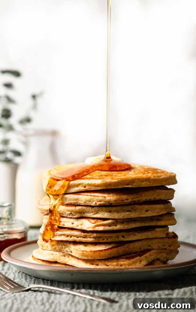 Stack of pancakes on plate with syrup being poured over top.
