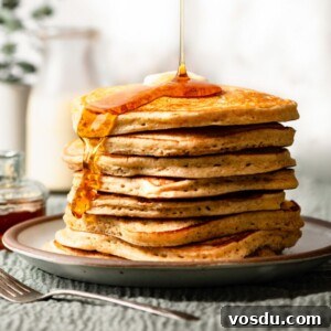 Stack of eggnog pancakes on a plate, topped with butter and maple syrup.
