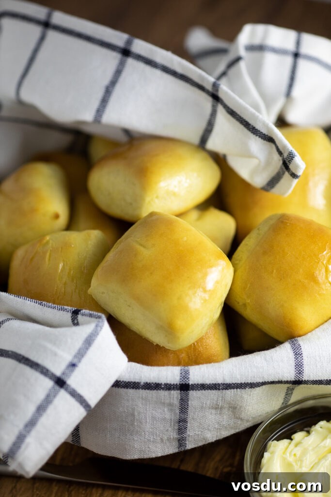 How to Make Texas Roadhouse-Style Rolls at Home 2 Texas Roadhouse Rolls in a bowl with a striped linen on a rustic wood background next to a small glass bowl of whipped butter.