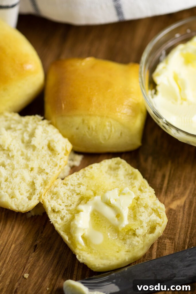 How to Make Texas Roadhouse-Style Rolls at Home 3 A copycat Texas Roadhouse roll cut in half with melted butter smeared on top on a rustic wood background