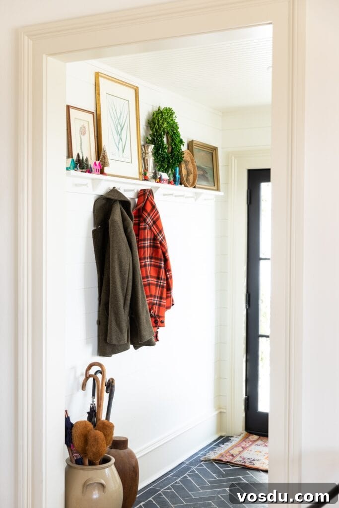 This Year’s Holiday Home Decor: Fresh Ideas to Transform Your Space 2 Looking into an entryway with black tile floor with pegs on the wall and coats hanging up with shelves adorned with Christmas decor