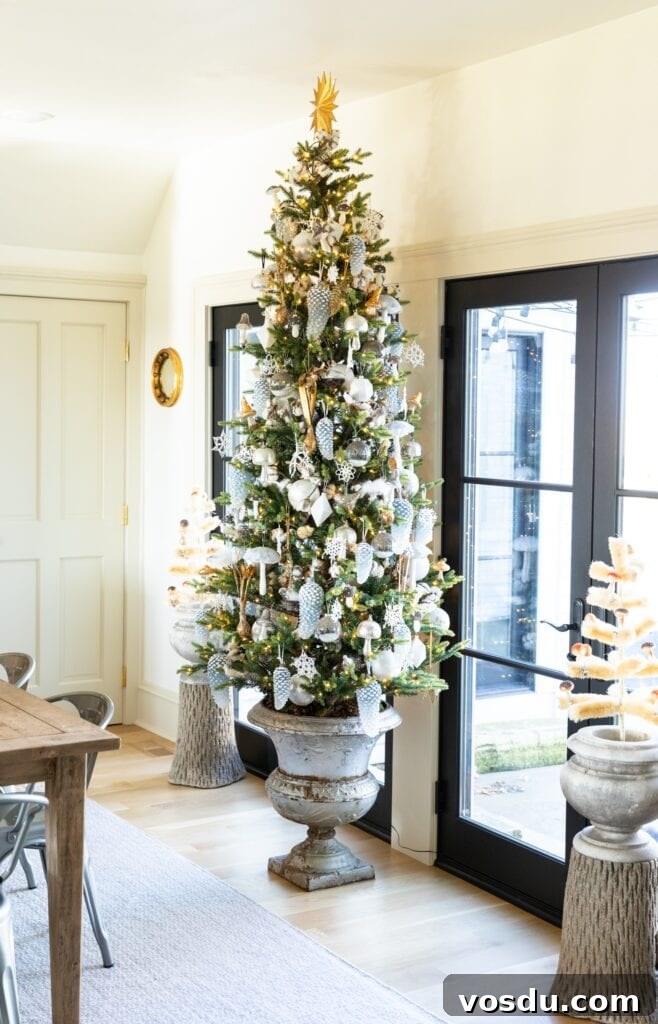 This Year’s Holiday Home Decor: Fresh Ideas to Transform Your Space 16 Large Christmas tree in concrete urn sitting in dining room covered in golds and silvers with black French doors behind leading onto patio