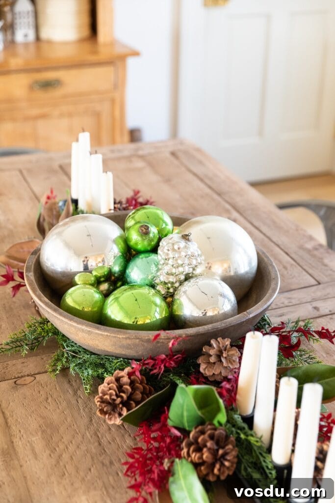 This Year’s Holiday Home Decor: Fresh Ideas to Transform Your Space 19 Wooden basket on wooden table filled with green and silver glass Christmas ornaments with greenery and candles all around