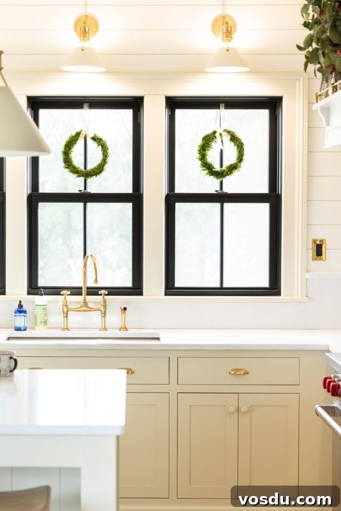 This Year’s Holiday Home Decor: Fresh Ideas to Transform Your Space 22 Two windows with green wreaths hanging from tops in white kitchen with white countertops and off-white cabinetry