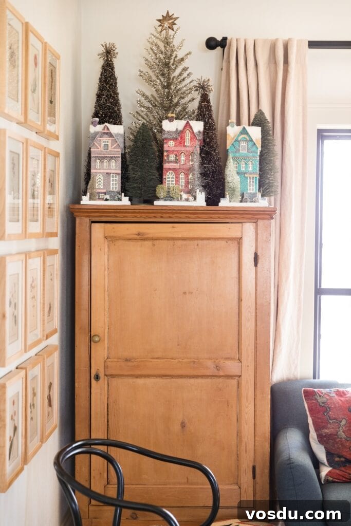 This Year’s Holiday Home Decor: Fresh Ideas to Transform Your Space 5 Pine chest topped with tall Christmas houses along with trees behind with couch to the side and frames on the wall on the other