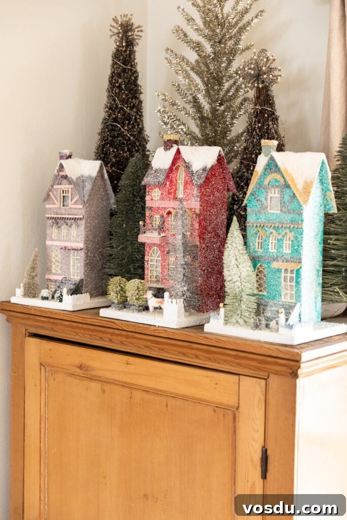 This Year’s Holiday Home Decor: Fresh Ideas to Transform Your Space 6 Three tall display Christmas houses with yards covered in snow sitting on top of pine dresser with trees in background