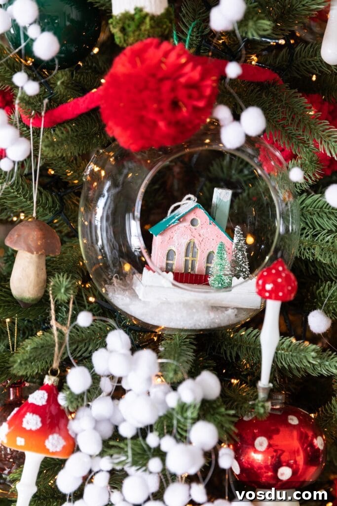 This Year’s Holiday Home Decor: Fresh Ideas to Transform Your Space 9 Close up view of glass dome with small pink paper house inside surrounded by mushroom ornaments on a Christmas tree