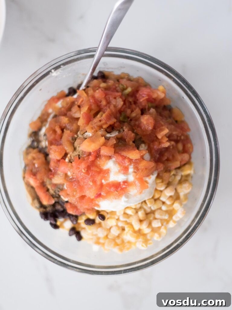 Tomatoes topping the corn and sour cream mixture in a mixing bowl.