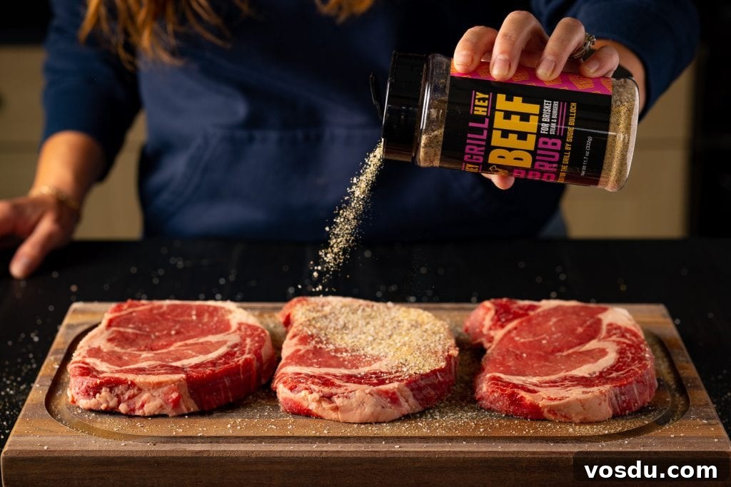 Three ribeye steaks being seasoned with Hey Grill Hey Beef Rub.