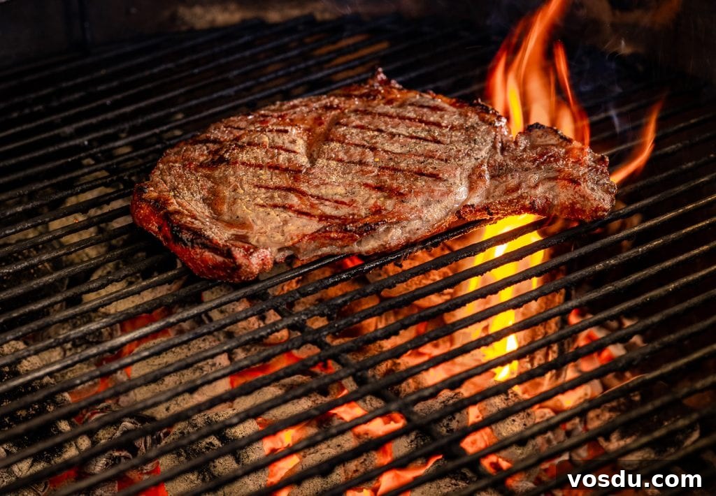Seasoned ribeye steak over direct heat on a charcoal grill.