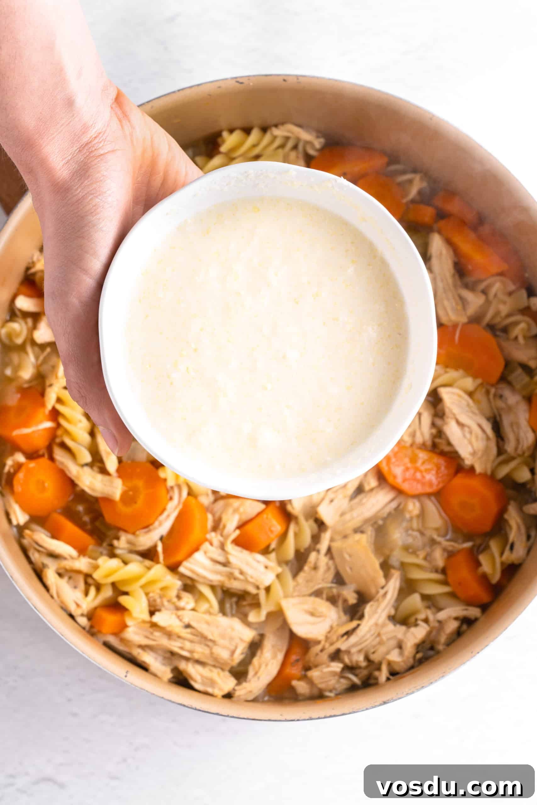 Gluten-Free Chicken Noodle Soup Recipe (Dairy-Free) Holding a bowl of slurry over a pot of chicken noodle soup.