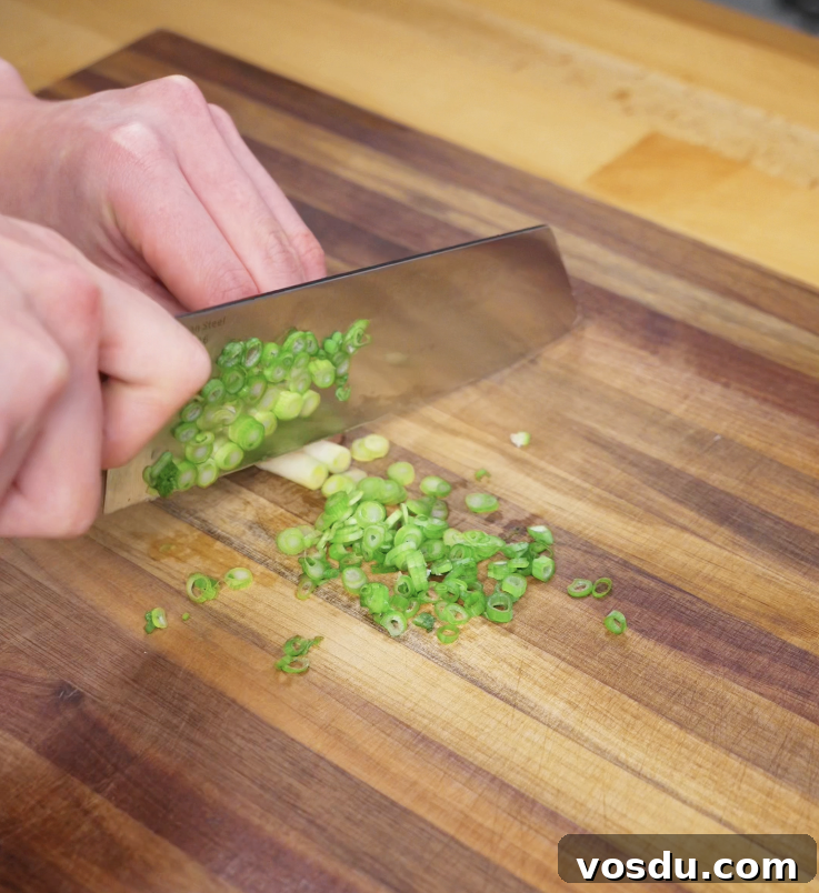Korean Corn Cheese Recipe: Creamy Cheesy Corn Bake Tutorial 4 Close-up of hands finely chopping scallions on a wooden cutting board, preparing garnish for Korean corn cheese.