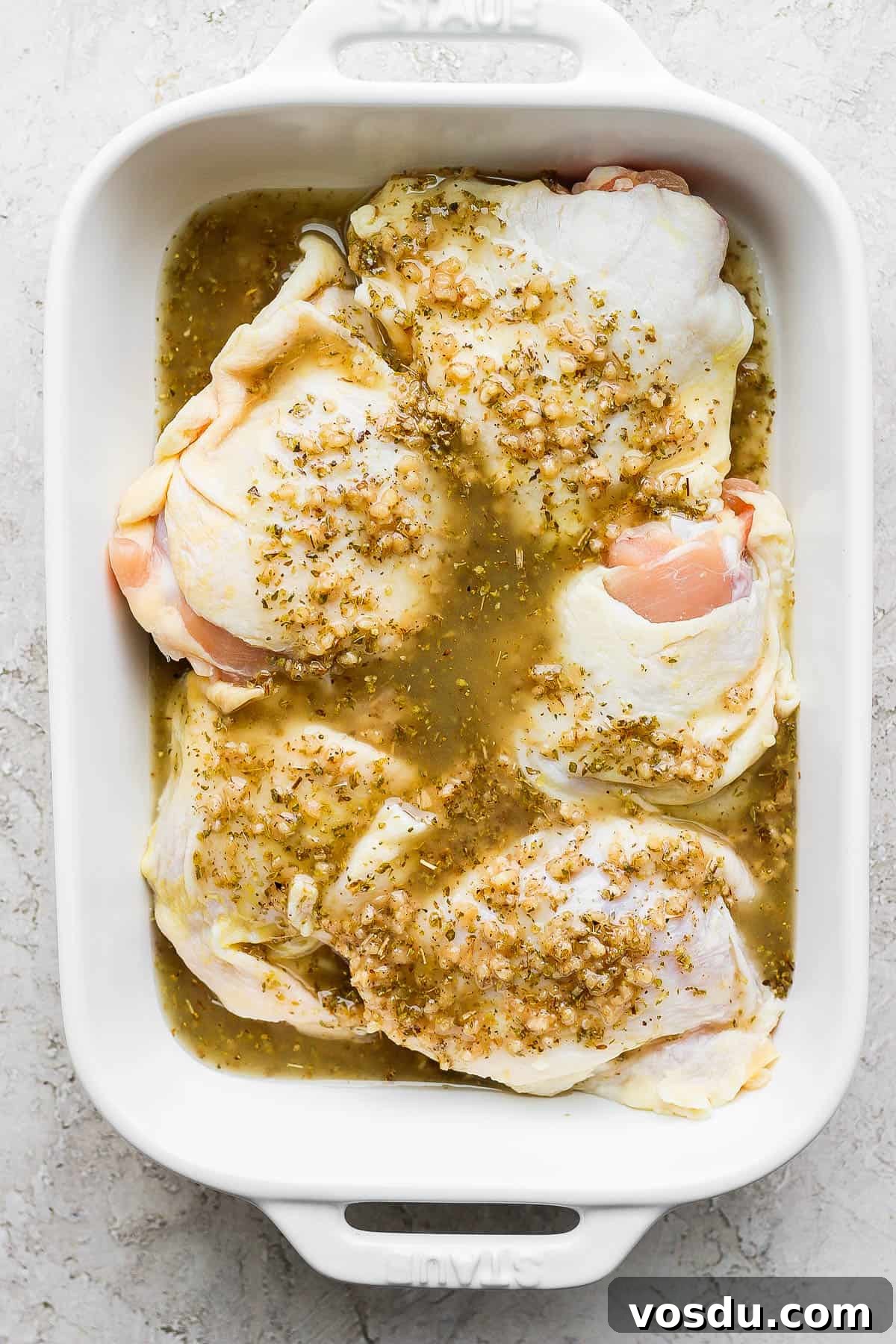 Greek-Style Chicken Marinade for Juicy, Flavorful Grilled Chicken 2 Bone-in, skin on chicken thighs in a casserole dish covered in Greek marinade.