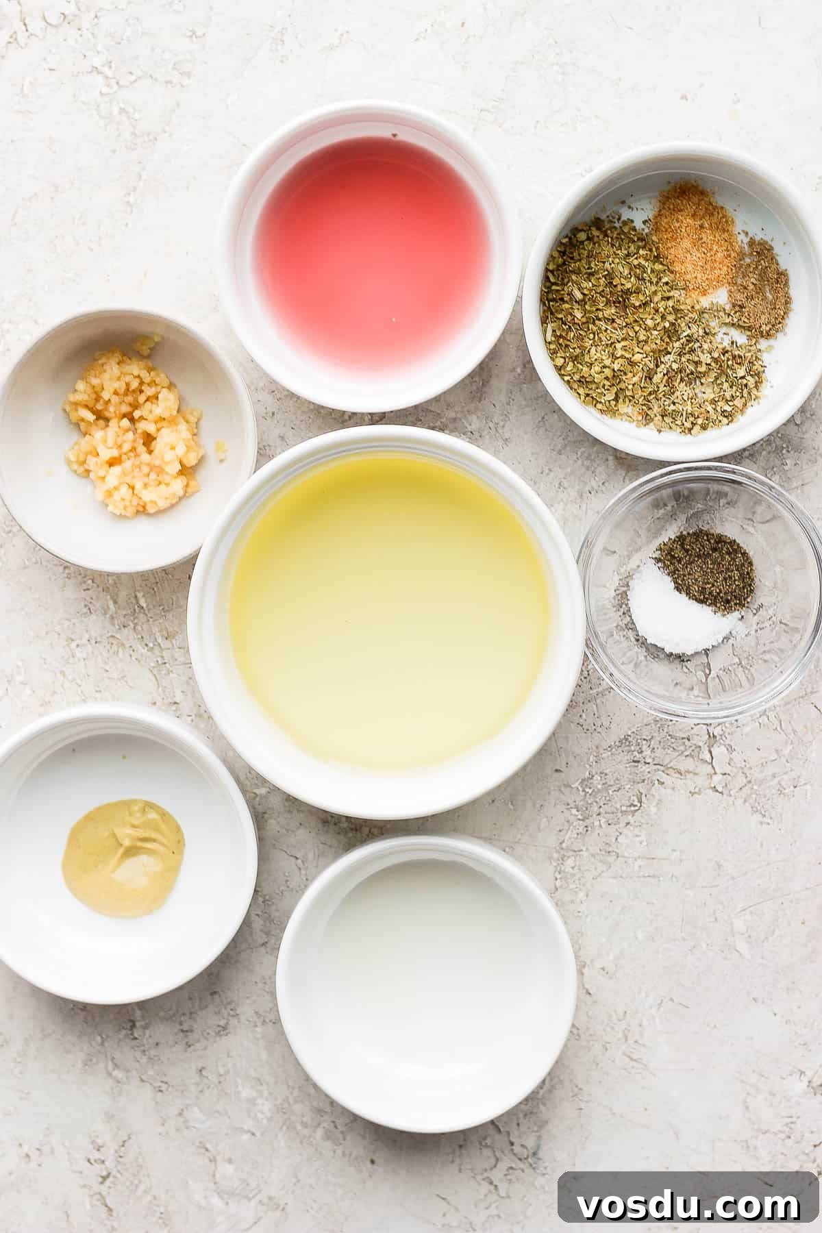 Greek-Style Chicken Marinade for Juicy, Flavorful Grilled Chicken 3 Seven small bowls, each with measured marinade ingredients; minced garlic, dijon mustard, salt and pepper, red wine vinegar, lemon juice, olive oil, oregano, coriander, and garlic powder.
