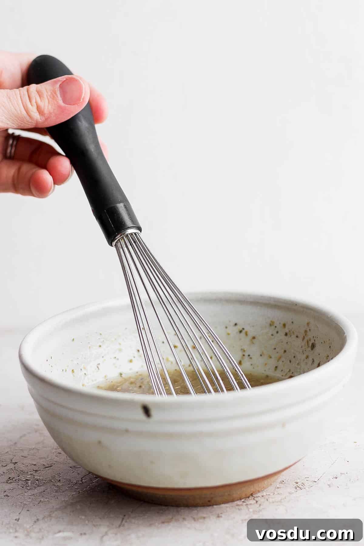 Greek-Style Chicken Marinade for Juicy, Flavorful Grilled Chicken 5 A hand holding a whisk in the small mixing bowl holding the marinade ingredients.