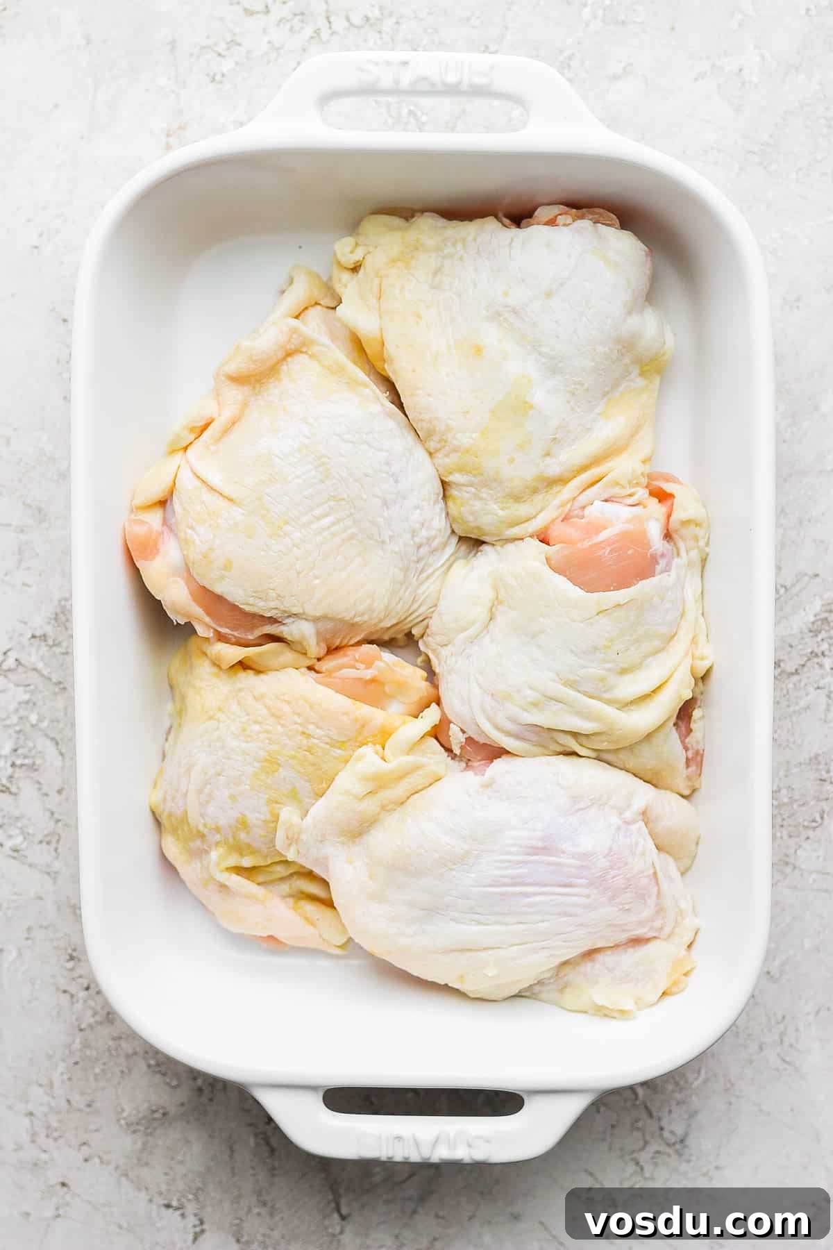 Greek-Style Chicken Marinade for Juicy, Flavorful Grilled Chicken 6 Five raw bone-in, skin on chicken thighs in a casserole dish.