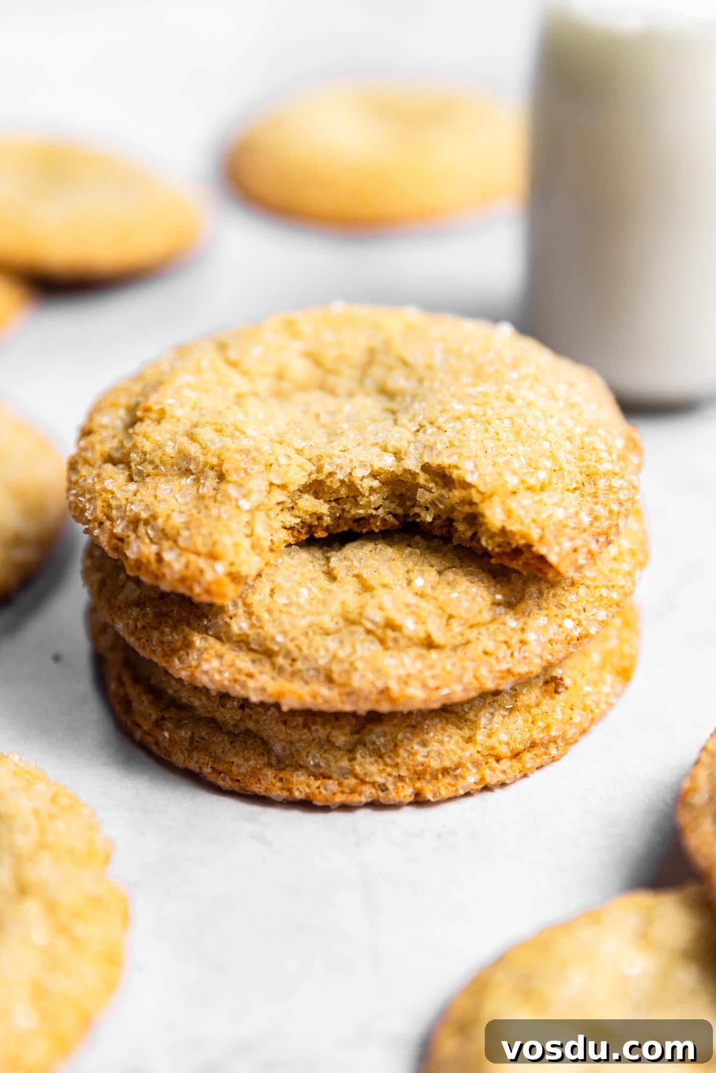 Simple Drop-Style Vanilla Sugar Cookies for Homemade Treats 3 Sugar cookies stacked on top of each other next to a glass of milk. There's a bite missing from the top cookie.