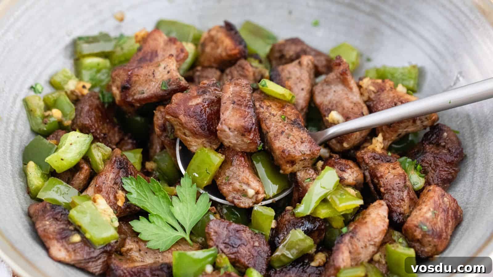 Sautéed diced meat with green peppers and herbs in a pan.