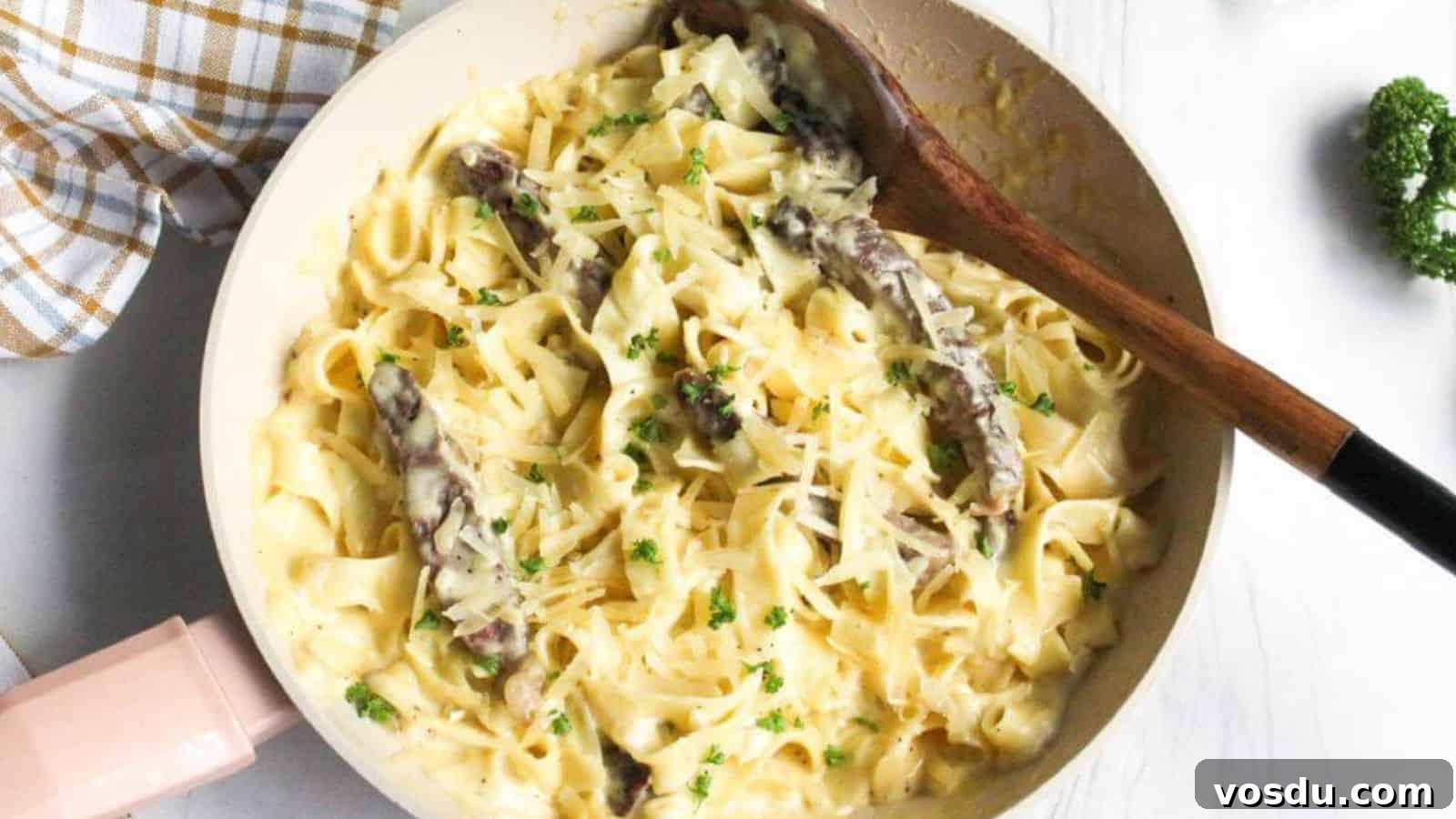 Alfredo steak pasta in skillet with wooden spoon.