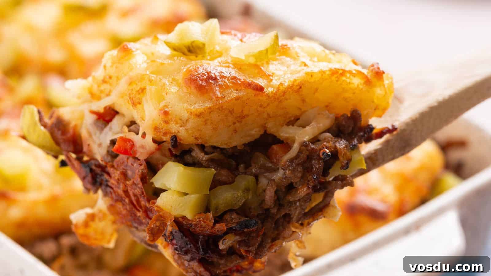 A close-up of a serving spoon lifting a portion of sloppy joe casserole showing layers of ground meat, vegetables, and golden-brown hashbrown potatoes.