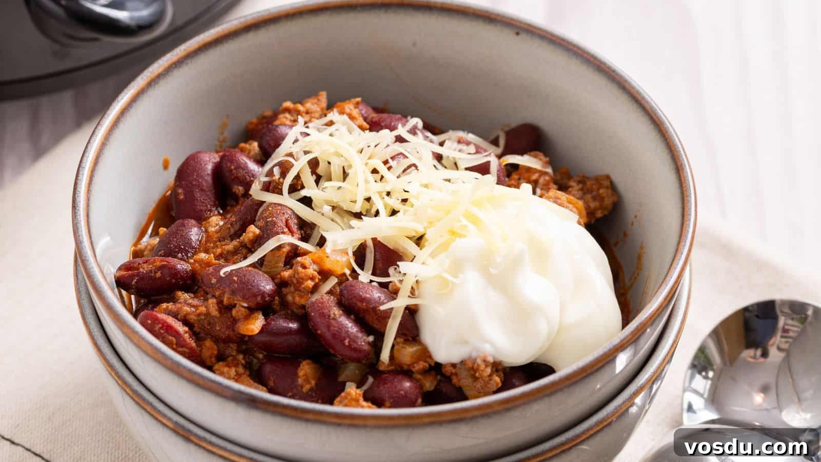 Bowl of chili with shredded cheese and a dollop of sour cream on top.