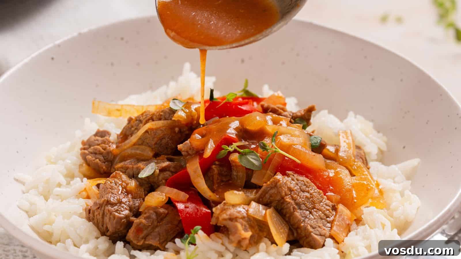 Sauce being poured over a bowl of beef and bell pepper stir-fry served on white rice.
