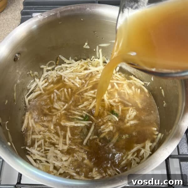 broth being added to shredded potatoes and softened onions