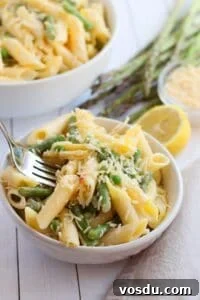 Chilled Asparagus and Tomato Salad with Lemon Vinaigrette 6 A bowl of Lemon Asparagus Pasta features penne mixed with asparagus and topped with grated cheese, accompanied by a fork, lemon, and fresh asparagus spears in the background.
