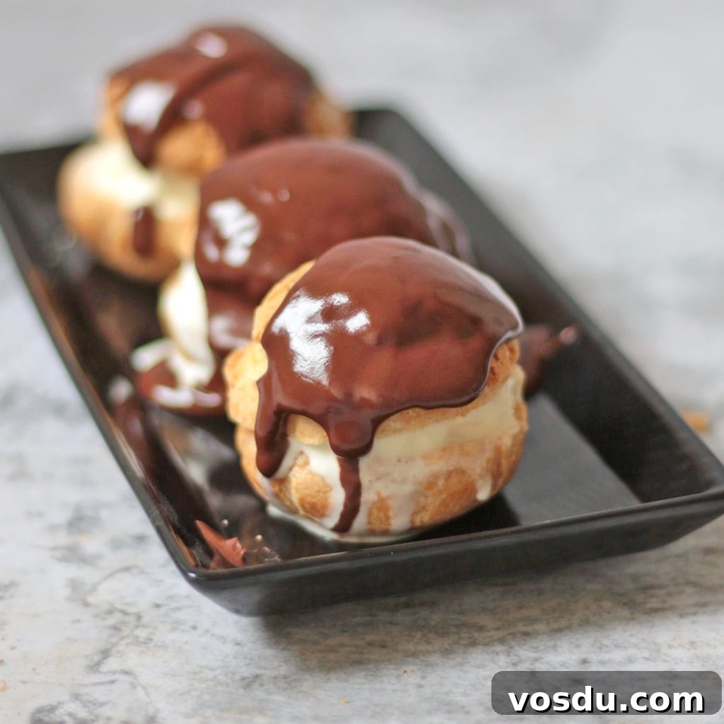 Classic French Profiteroles with Rich Chocolate Sauce 2 3 profiteroles with chocolate sauce on a black plate.