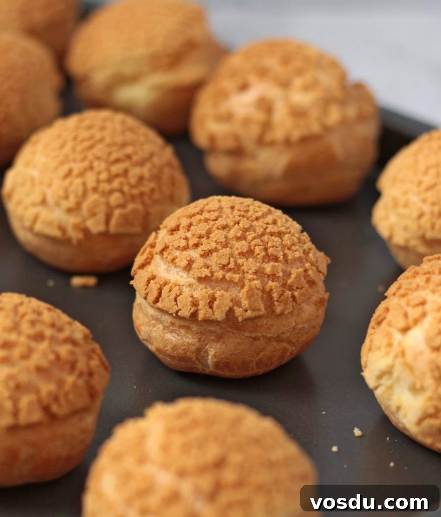 Classic French Profiteroles with Rich Chocolate Sauce 3 Choux Buns with Craquelin topping on a baking tray.