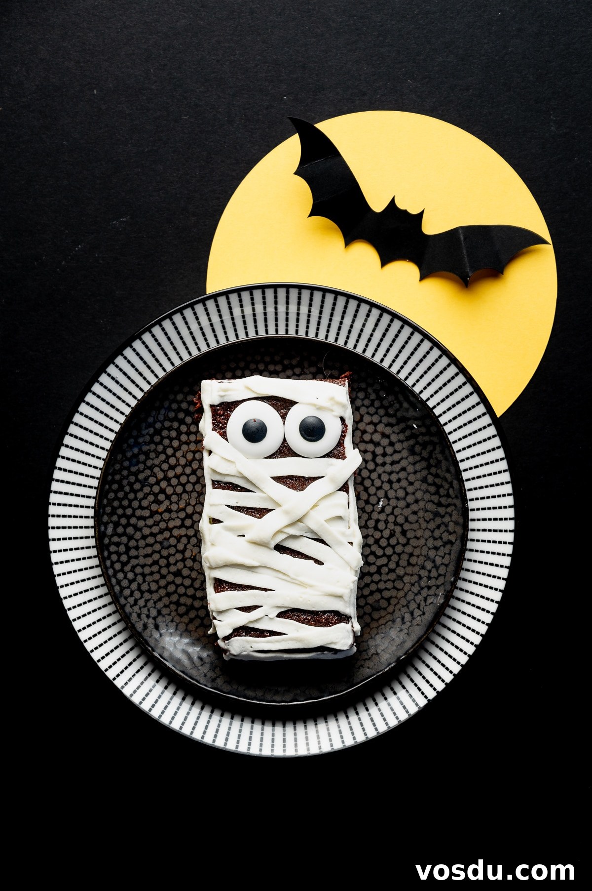 Halloween Mummy Sugar-Free Brownies — Gluten-Free Low-Carb Treats 3 Sugar free brownie with googly eyes and frosting applied in strips to look like bandages on a black background with a bright yellow paper moon and paper bat