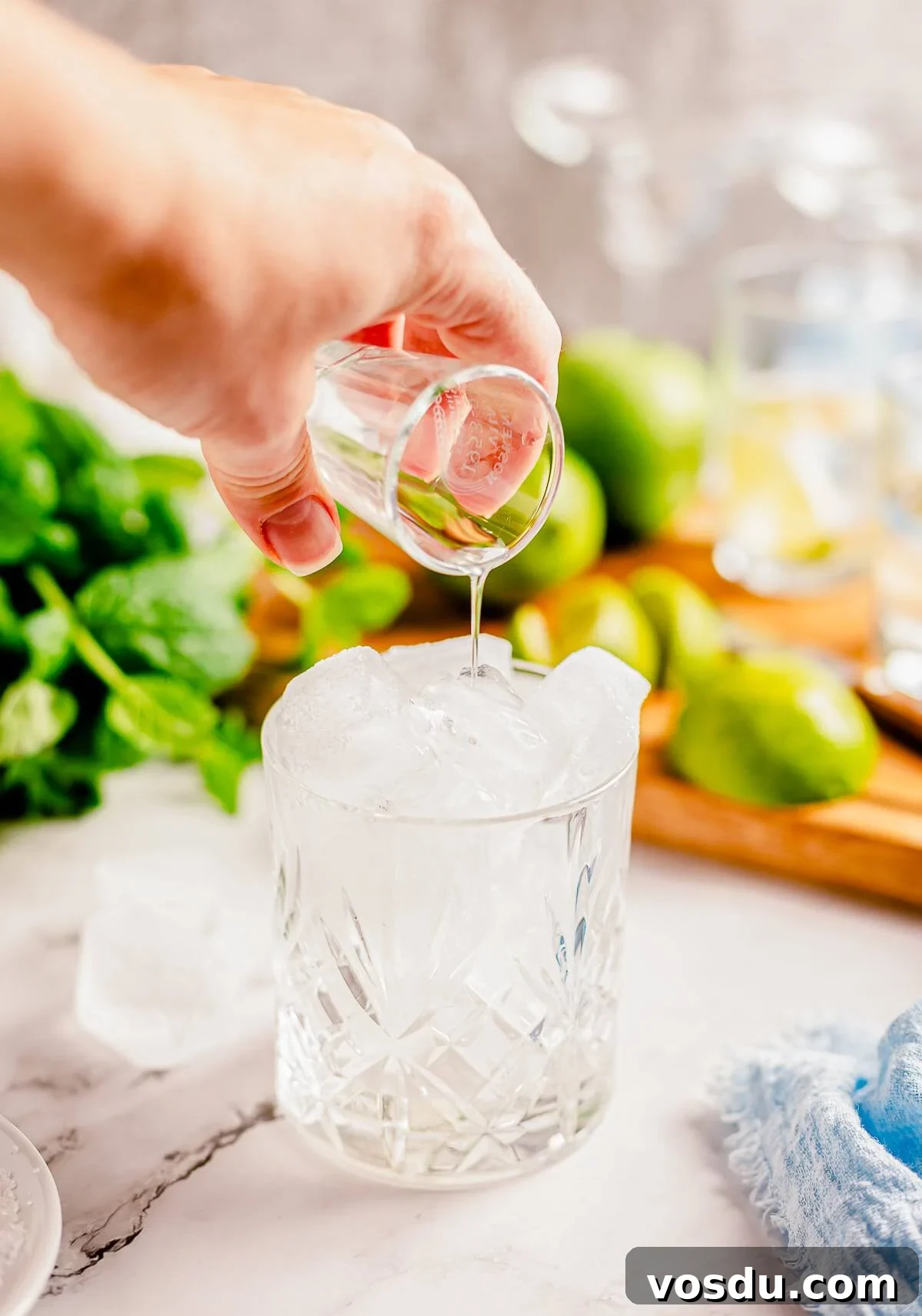 A shot glass being poured with simple syrup into a glass of ice