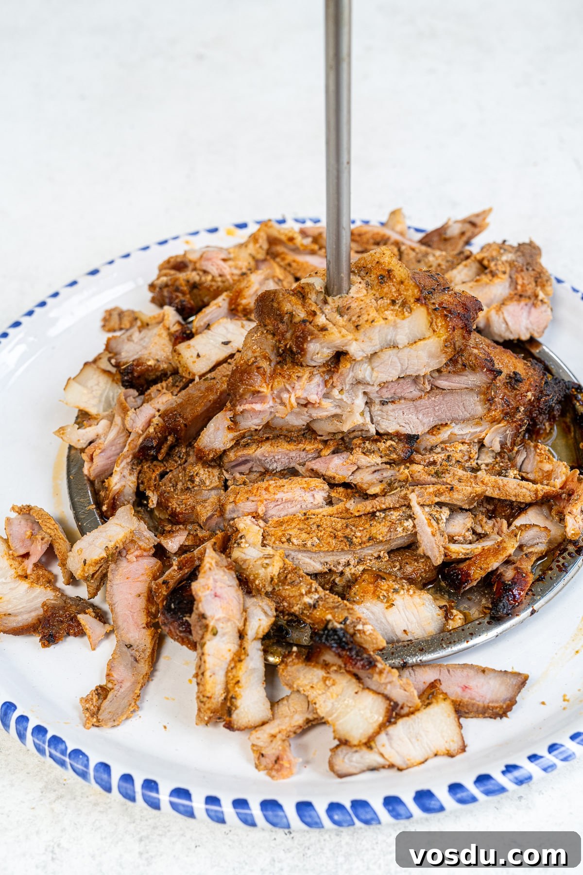 Crispy Air Fryer Pork Gyros Recipe for Quick Weeknight Meals 2 A large plate of sliced, seasoned Air Fryer Pork Gyros stacked on a vertical skewer, ready to serve in true authentic Greek recipe style, with a blue and white rimmed plate on a light surface.