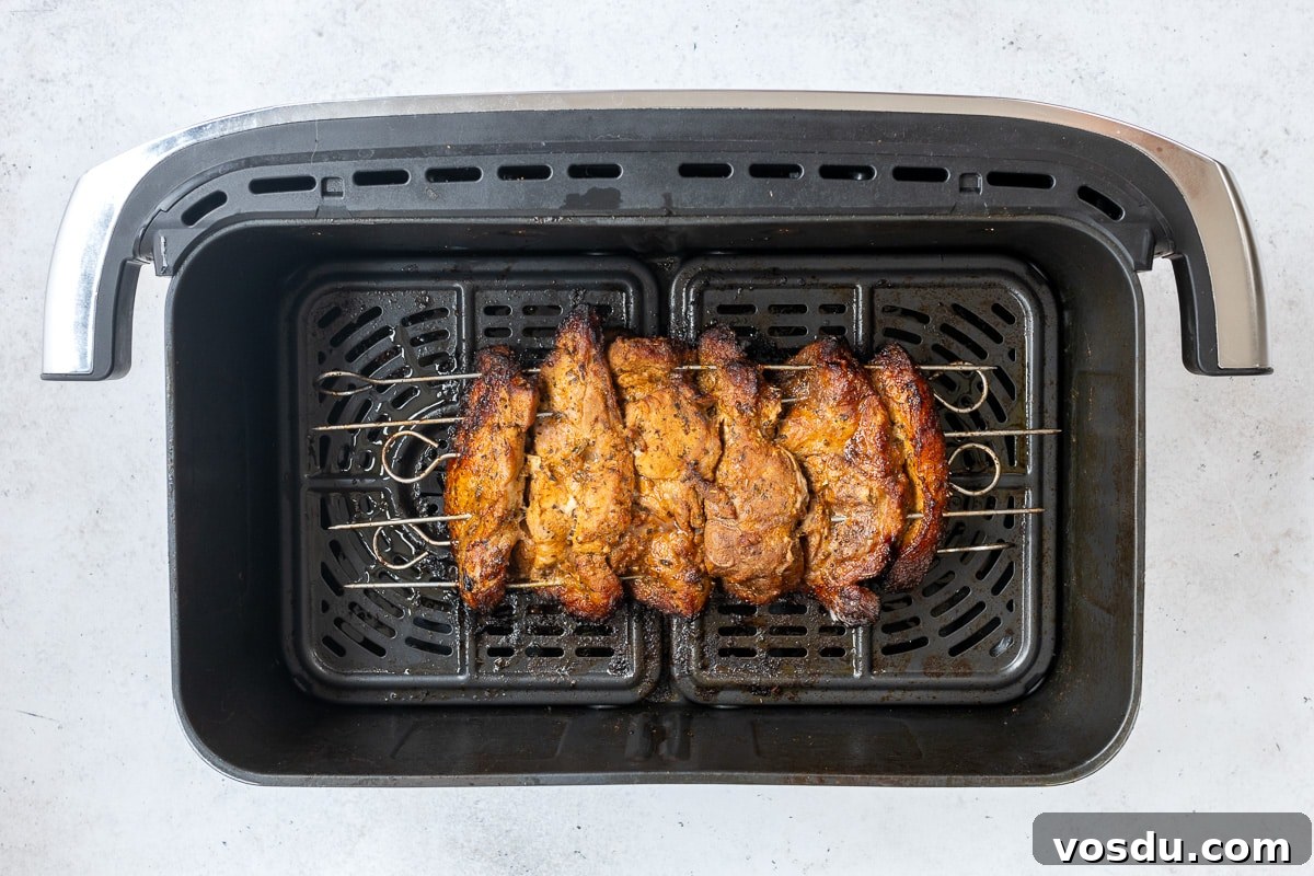 Crispy Air Fryer Pork Gyros Recipe for Quick Weeknight Meals 10 Five skewers with seasoned, grilled meat for Air Fryer Pork Gyros are placed inside an air fryer basket on a light surface, showing a cooked, golden-brown exterior reminiscent of an authentic Greek recipe.