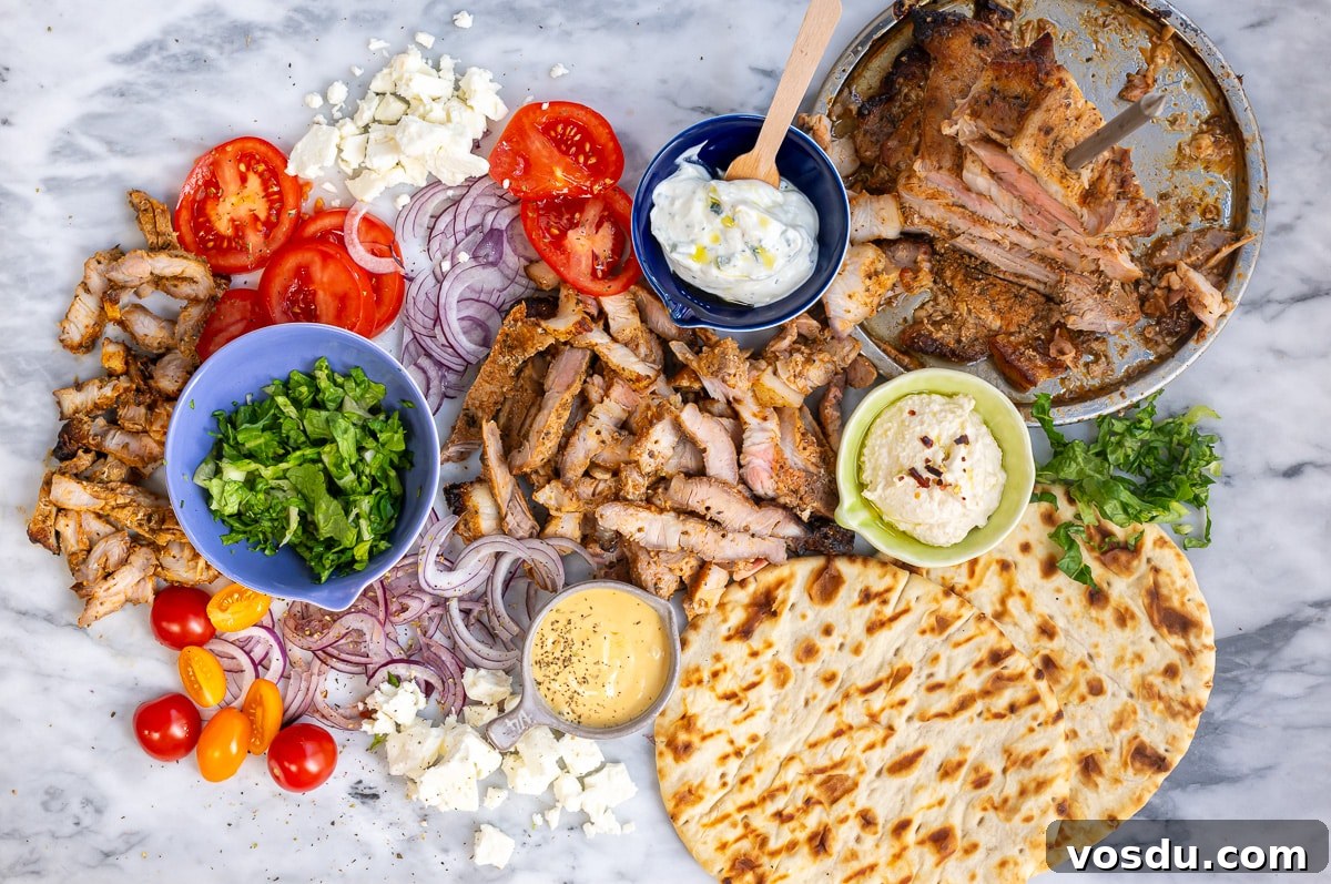Crispy Air Fryer Pork Gyros Recipe for Quick Weeknight Meals 11 A spread of sliced Air Fryer Pork Gyros, pita bread, tomato, onion, feta cheese, lettuce, tzatziki, hummus, and yellow sauce on marble—arranged for assembling authentic Greek wraps or gyros.