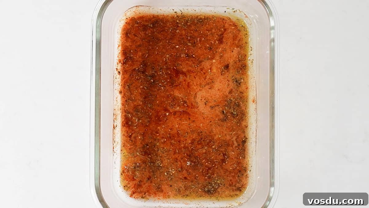Crispy Air Fryer Pork Gyros Recipe for Quick Weeknight Meals 5 A glass baking dish containing a reddish-brown marinade with visible herbs and spices, perfect for preparing authentic Greek recipe Pork Gyros, viewed from above on a white background.