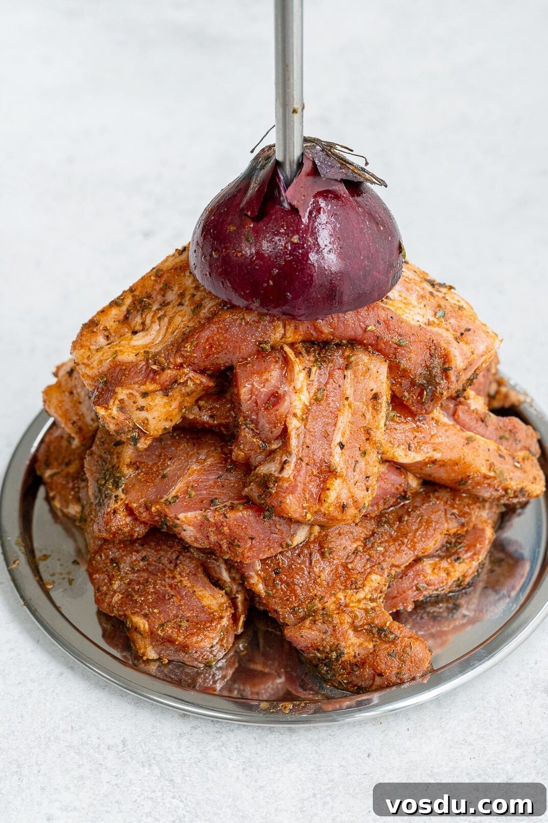 Crispy Air Fryer Pork Gyros Recipe for Quick Weeknight Meals 6 A stack of marinated pork gyros slices arranged on a round metal tray, topped with half a red onion skewered by a vertical metal rod, captures the essence of an authentic Greek recipe.