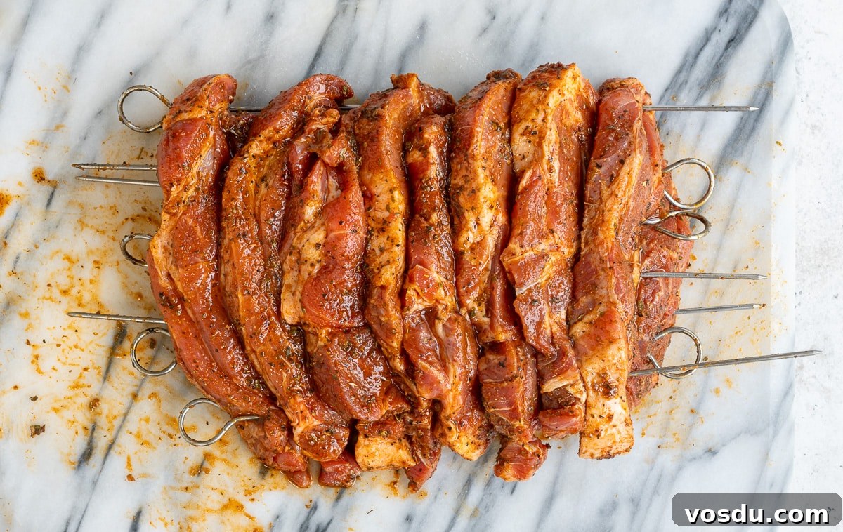 Crispy Air Fryer Pork Gyros Recipe for Quick Weeknight Meals 7 Raw marinated pork skewers, prepared for grilling, are arranged side by side on a marble surface. Seasoned with spices and placed on metal skewers, these are perfect for making authentic Greek recipe Pork Gyros.
