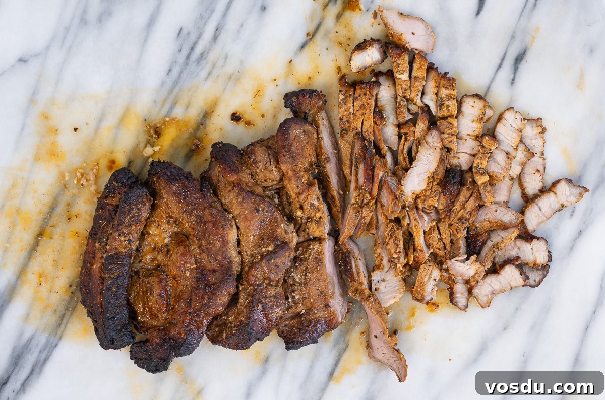 Crispy Air Fryer Pork Gyros Recipe for Quick Weeknight Meals 8 A cooked, seasoned pork roast rests on a white marble surface, with part of it sliced into thin strips—perfect for Pork Gyros. The meat looks juicy, with visible char and spices inspired by an authentic Greek recipe.