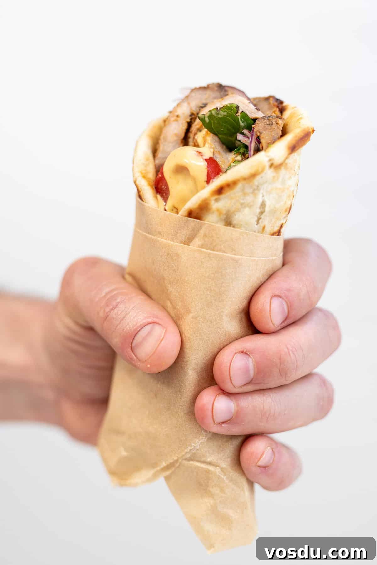 Crispy Air Fryer Pork Gyros Recipe for Quick Weeknight Meals 9 A hand holds a wrapped pita filled with air fryer pork gyros, leafy greens, sliced tomato, and sauce—an irresistible twist on an authentic Greek recipe—against a plain white background.